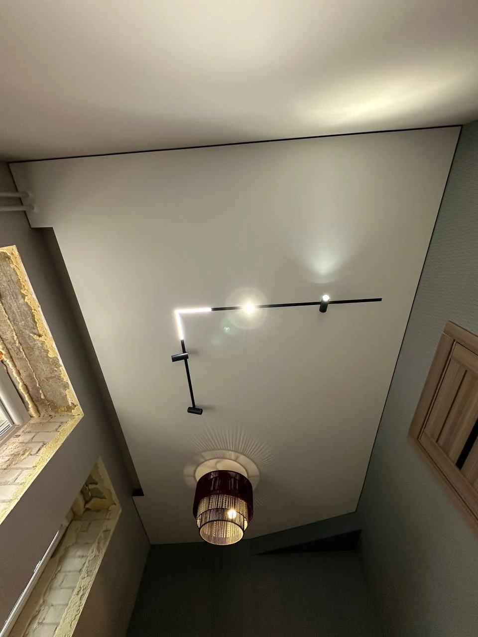 Матовый натяжной потолок в спальню со скрытым карнизом люстрой и врезным трековым освещением на теневом профиле