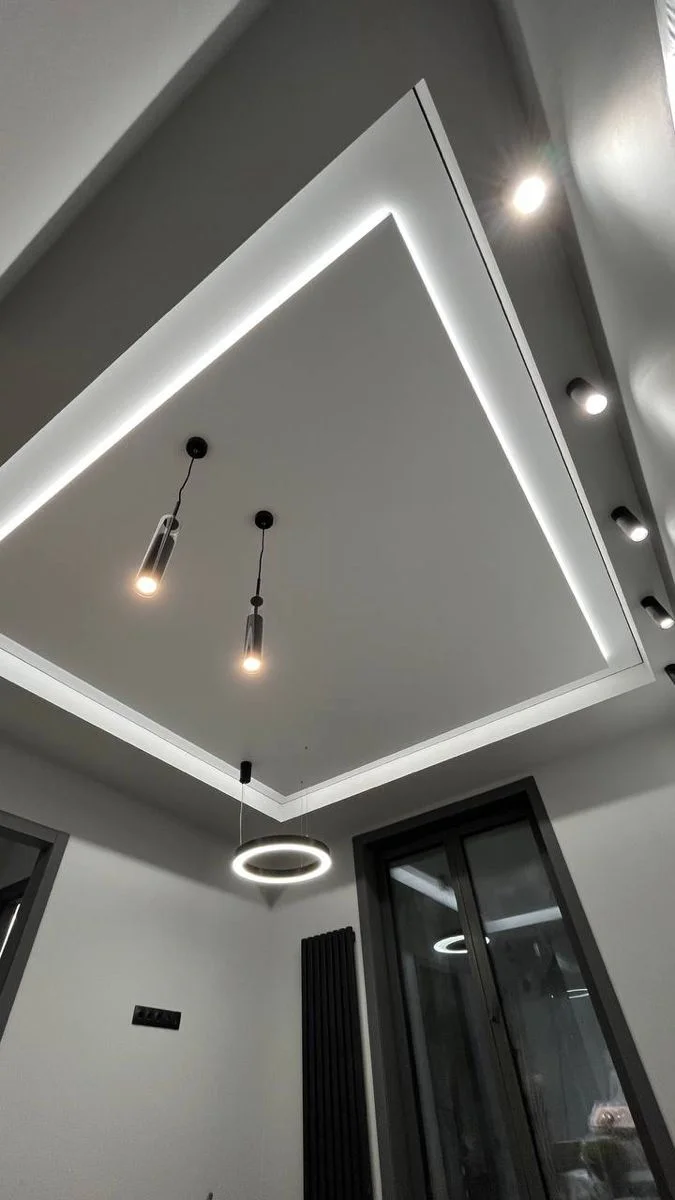 Многоуровневый матовый натяжной потолок с подсветкой накладными точечными светильниками и подвесными люстрами в частном доме