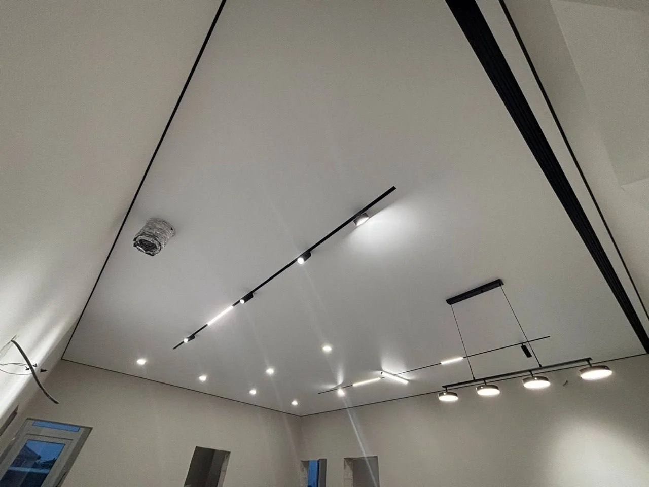 Матовый натяжной потолок в гостиную с двумя трековыми светильниками и люстрой